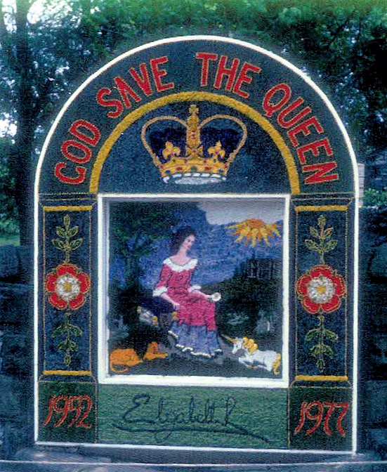 A well dressing depicting Elizabeth II with a small lion and unicorn nealt at her feet. The heading reads 'God Save The Queen'