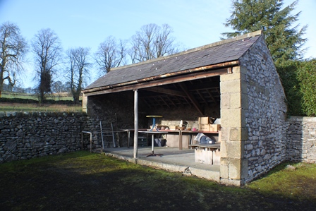 A picture of an old stone shed without a front. The shed contains various items which cannot be discerned.